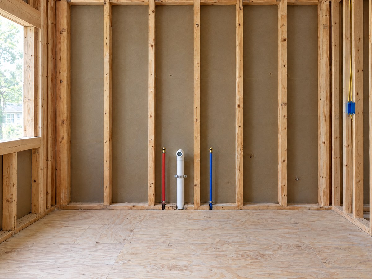 Illustration: a kitchen wall open to the studs, with the drain and supply lines visible before drywall